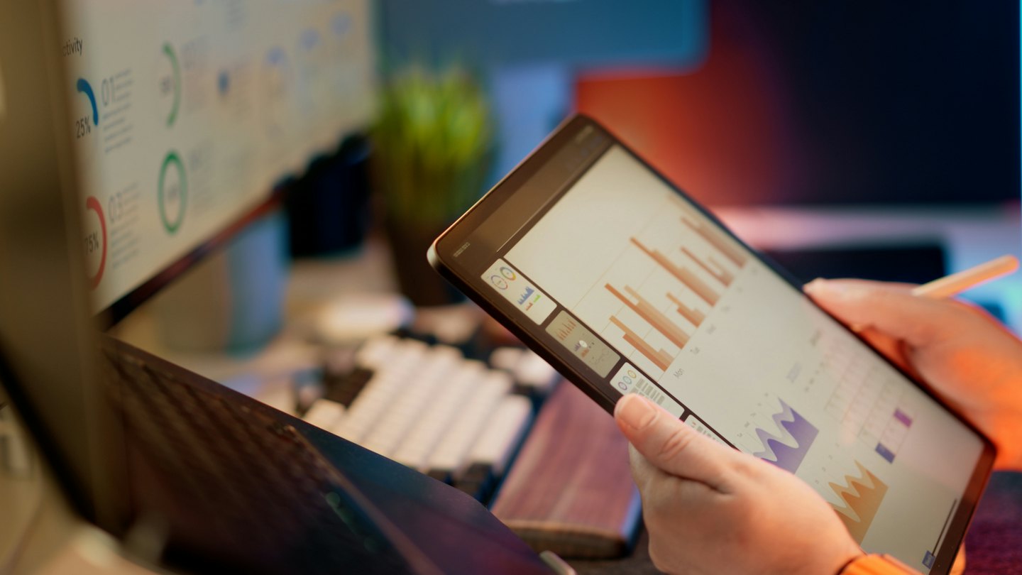 Osoba analyzujúca obchodné grafy na tablete pri stole.